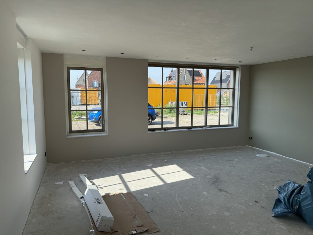 Lege woonkamer van een nieuwe woning met grote ramen en lichtgrijze wanden
